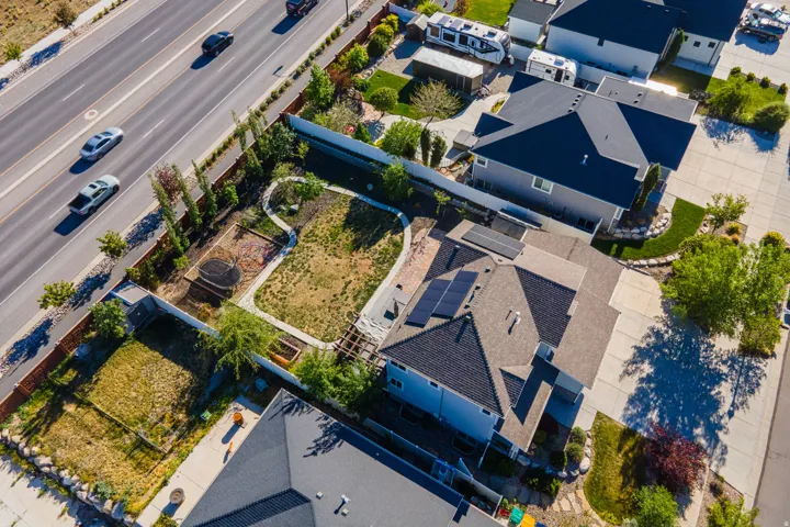 Aerial perspective showcasing a residential property with solar panels, a brown shingle roof, a light gray exterior, and a paved driveway
