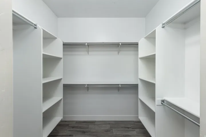 Walk-in closet featuring white built-in shelving, multiple hanging rods, and wood-finish flooring