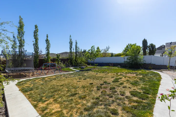 Spacious backyard featuring a manicured lawn, concrete pathway, and mature trees