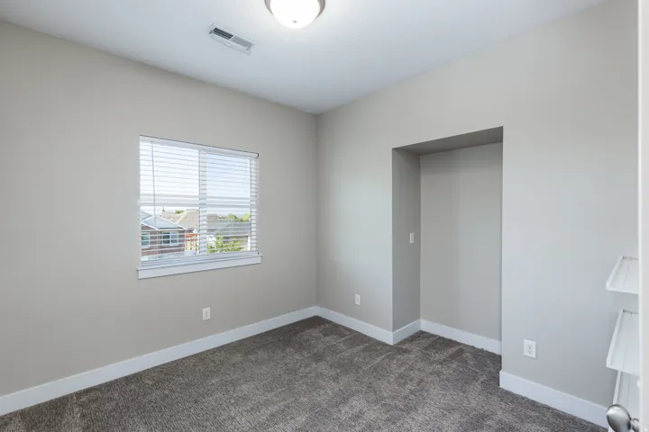 Carpeted room with a window featuring horizontal blinds, recessed wall alcove, and a flush mount ceiling light