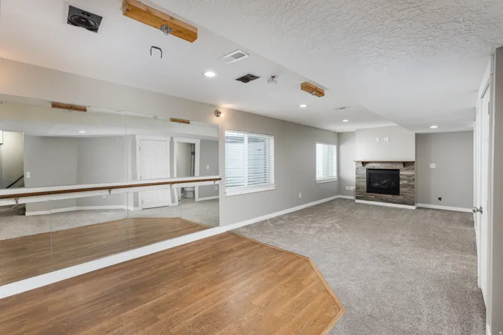 Recreation room featuring full-wall mirrors with a ballet barre, wood-finish flooring, recessed lighting, and a fireplace with a stacked stone surround