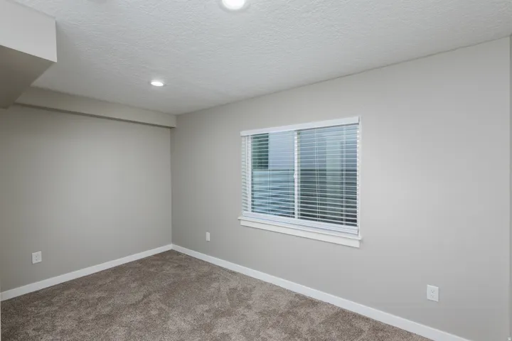 Carpeted room with a horizontal sliding window featuring white blinds, recessed lighting, and light gray wall paint with white trim
