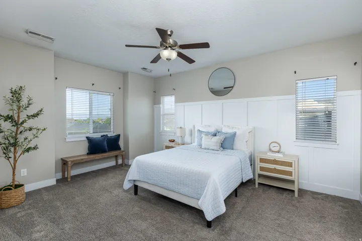 Bedroom featuring board and batten wall detailing, a ceiling fan with integrated lighting, two windows with blinds, and carpeted flooring