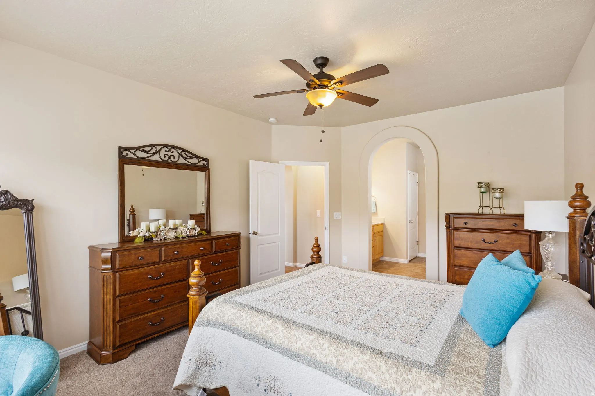 Large primary bedroom featuring a ceiling fan with integrated lighting, an arched doorway, and neutral wall tones