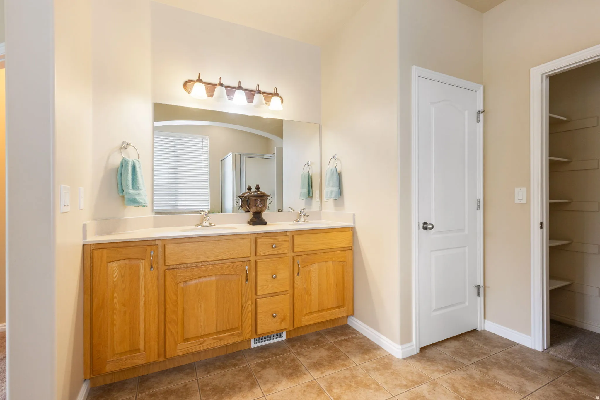 Spacious ensuite bathroom featuring a dual vanity with light-colored countertops, wood-finish cabinetry, and a large mirror