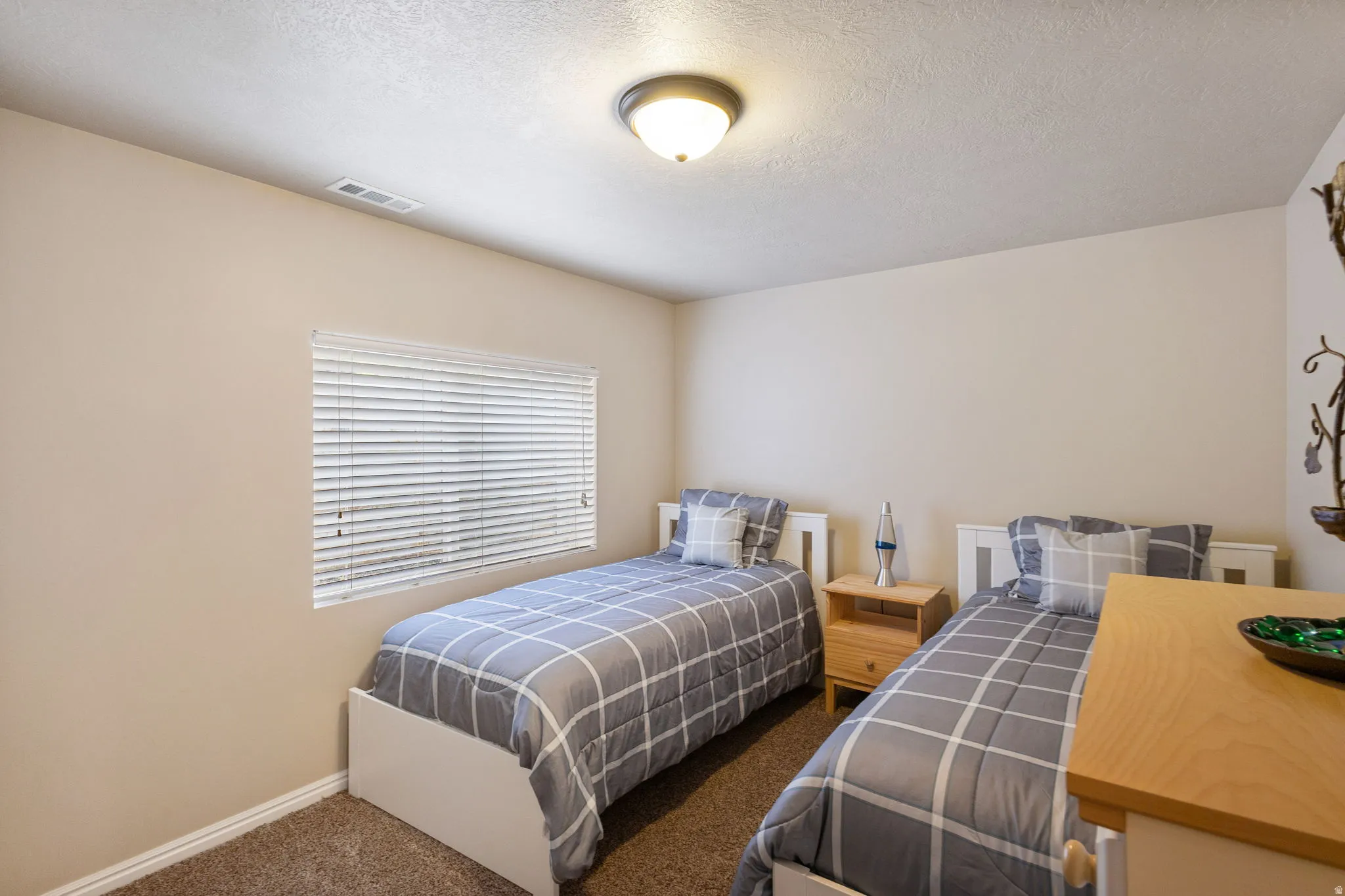 Neutral-toned room featuring a single window with horizontal blinds, textured ceiling, and a flush-mount light fixture