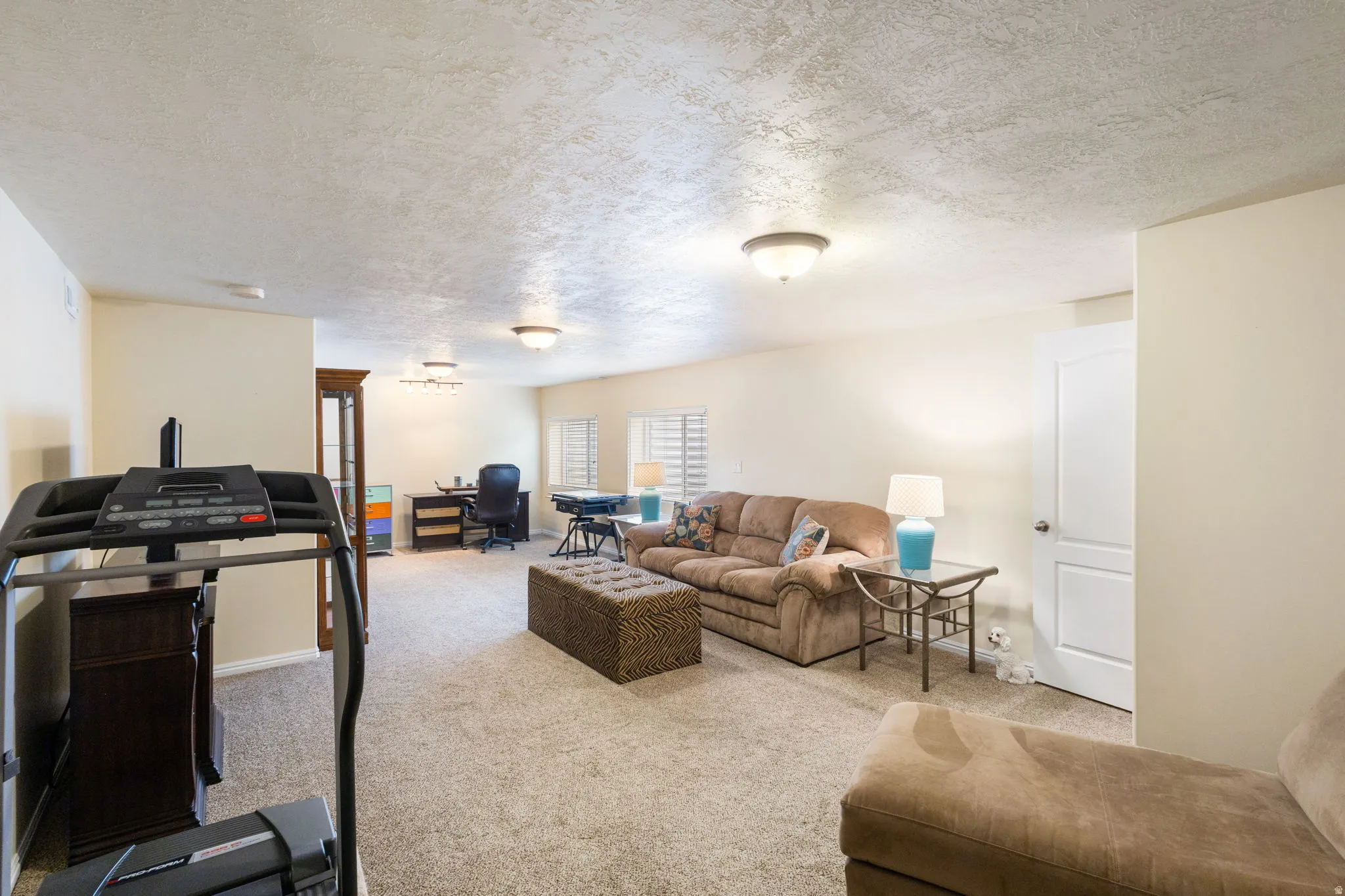 Spacious carpeted room featuring recessed lighting, multiple windows with horizontal blinds, and a built-in wall unit with glass doors