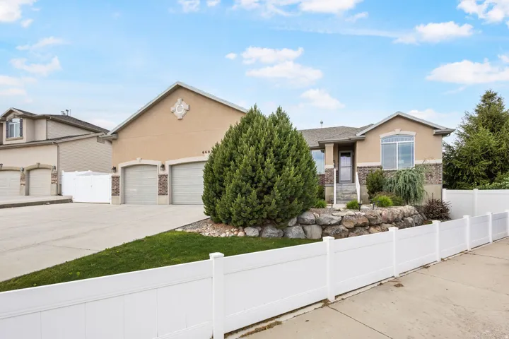 Contemporary stucco and stone exterior featuring a two-car garage, concrete driveway, and a white vinyl fence