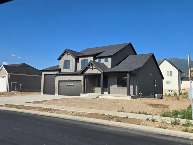 Contemporary two-story residence featuring a dark gray roof, two-car garage, covered porch entry, and a light gray siding exterior