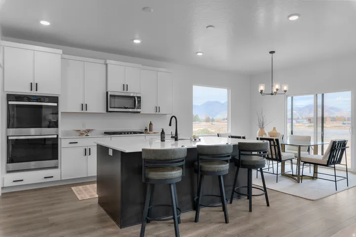 Open-concept kitchen featuring an oversized island with seating, stainless steel double wall ovens, a built-in microwave, white upper and lower cabinetry, and wood-finish flooring
