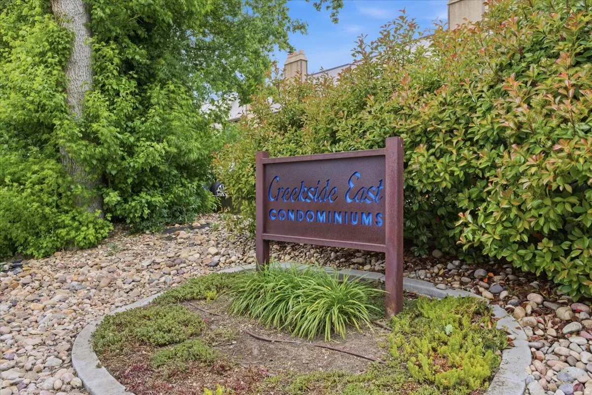 Entryway signage for Creekside East Condominiums, featuring a dark wood-finish sign with blue lettering