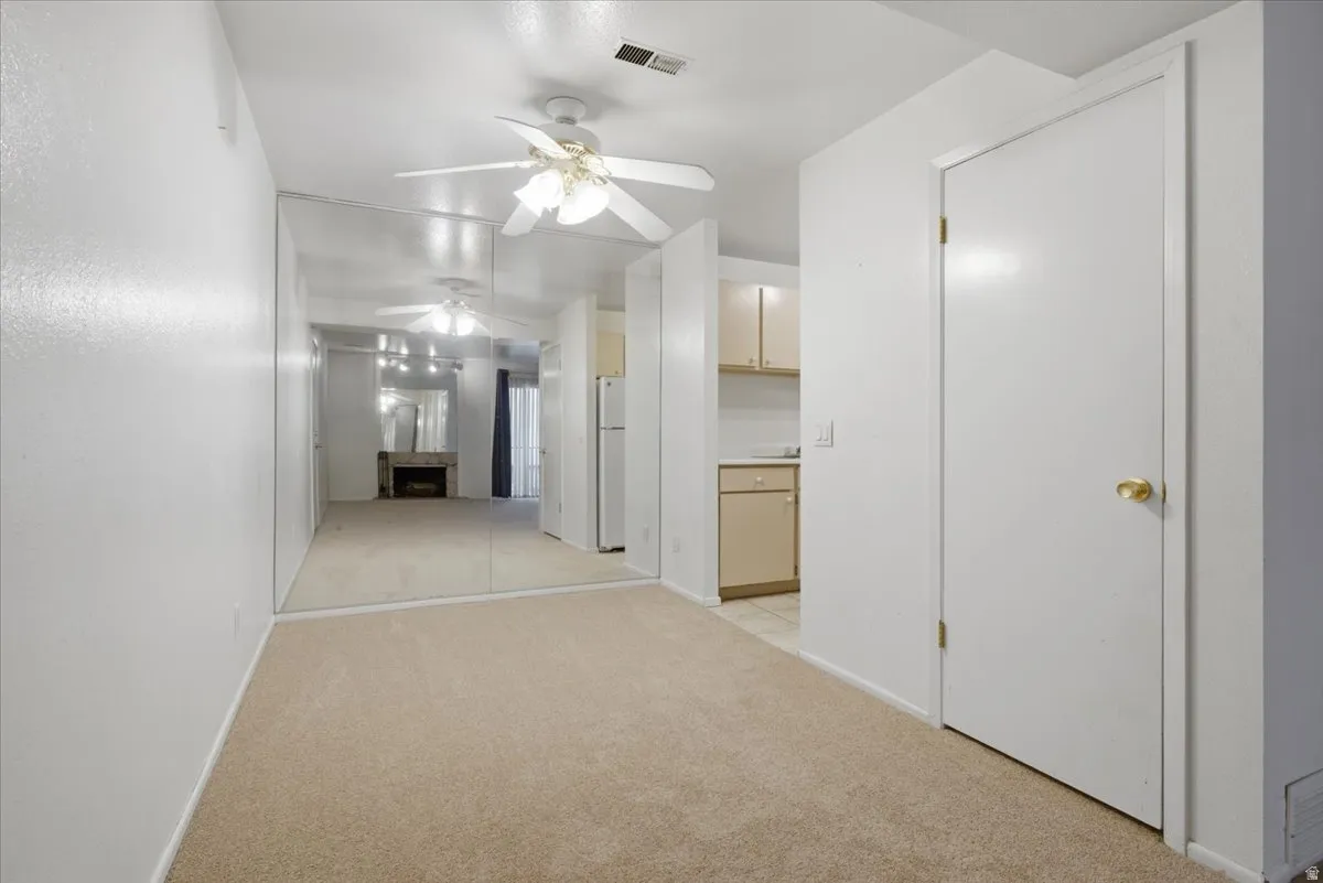 Carpeted living space featuring a ceiling fan, mirrored accent wall, and white painted walls