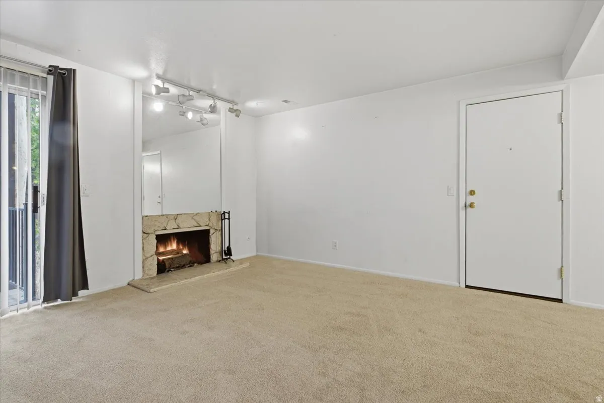 Living area featuring a stone-clad fireplace with hearth, mirrored wall accent, track lighting, and a sliding glass door leading to an exterior balcony