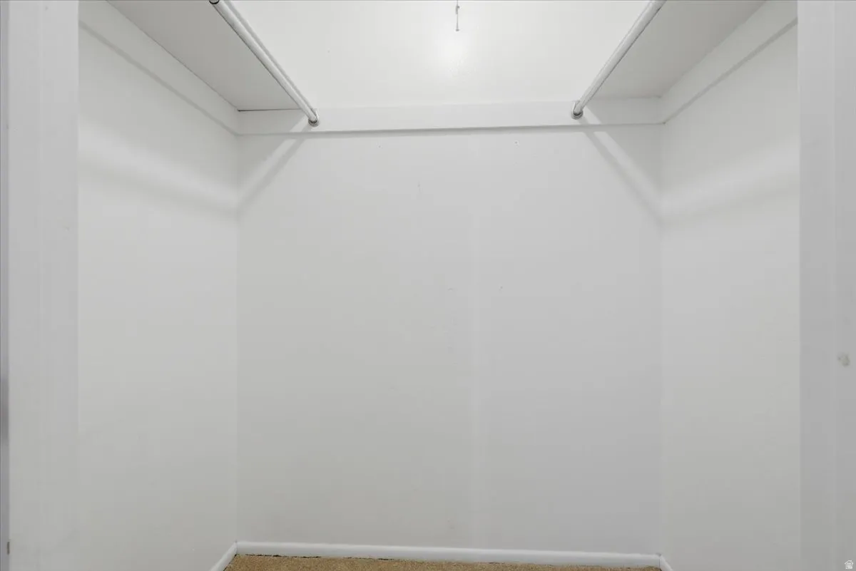 Walk-in closet with white walls, upper shelving, and hanging rods