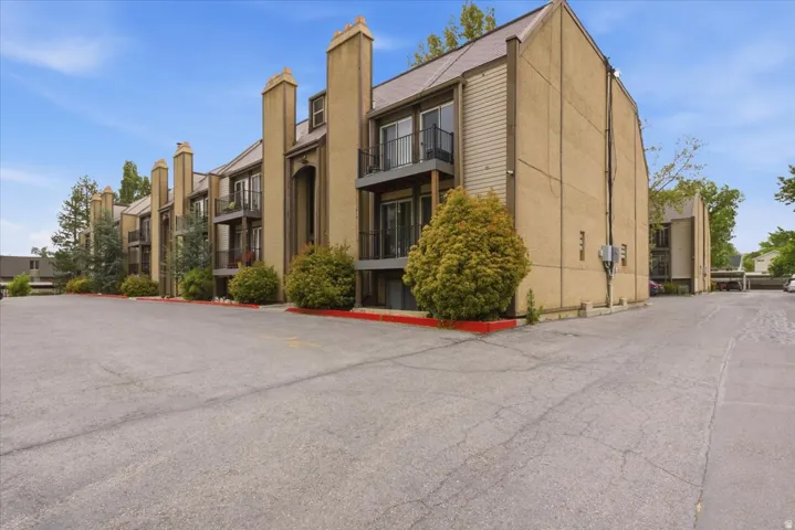 Multi-story building featuring balconies with black railings, exterior siding, and a sloped roofline
