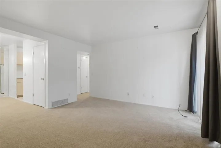 Spacious interior room featuring carpet flooring, white walls, and a large sliding glass door with dark drapes