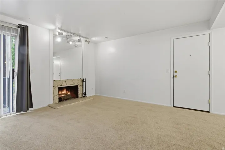 Living area featuring a stone-clad fireplace with hearth, mirrored wall accent, track lighting, and a sliding glass door leading to an exterior balcony