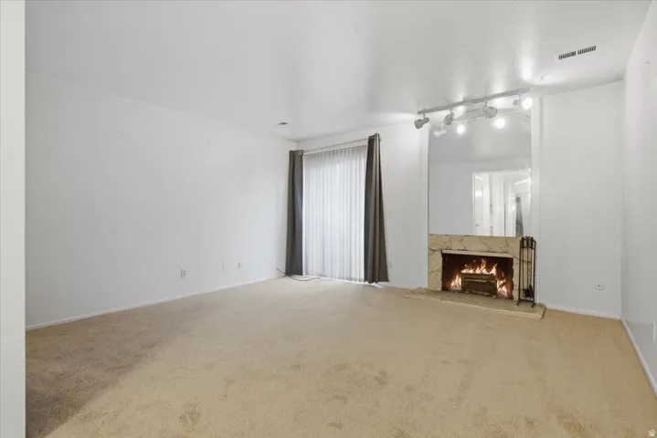 Spacious living area featuring a floor-to-ceiling mirrored accent wall with track lighting, a stone-clad fireplace, and neutral carpeting