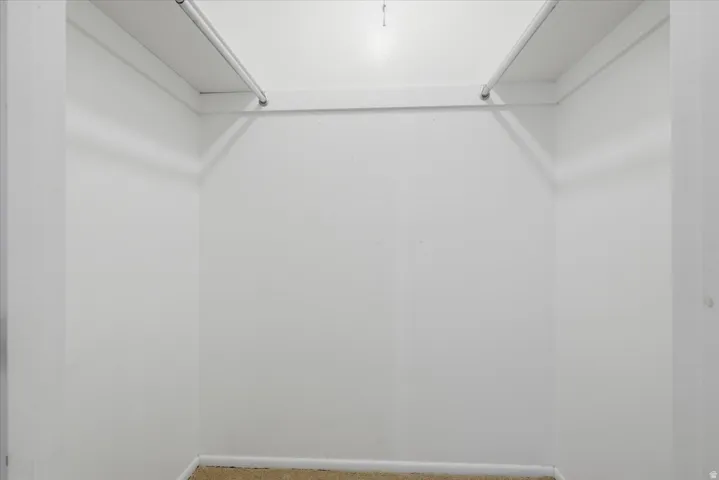 Walk-in closet with white walls, upper shelving, and hanging rods