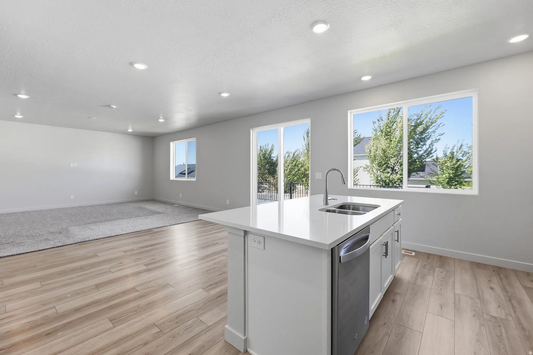 Open-concept living area featuring wood-finish flooring, recessed lighting, and a kitchen island with an integrated sink and stainless steel dishwasher