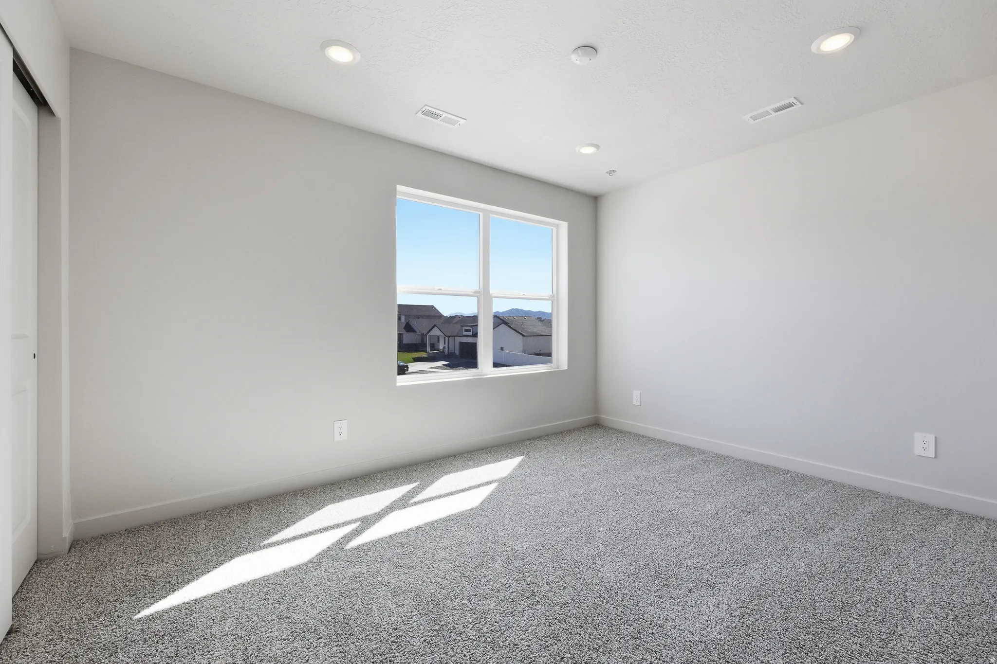 Spacious room featuring a large window, recessed lighting, and grey carpet flooring