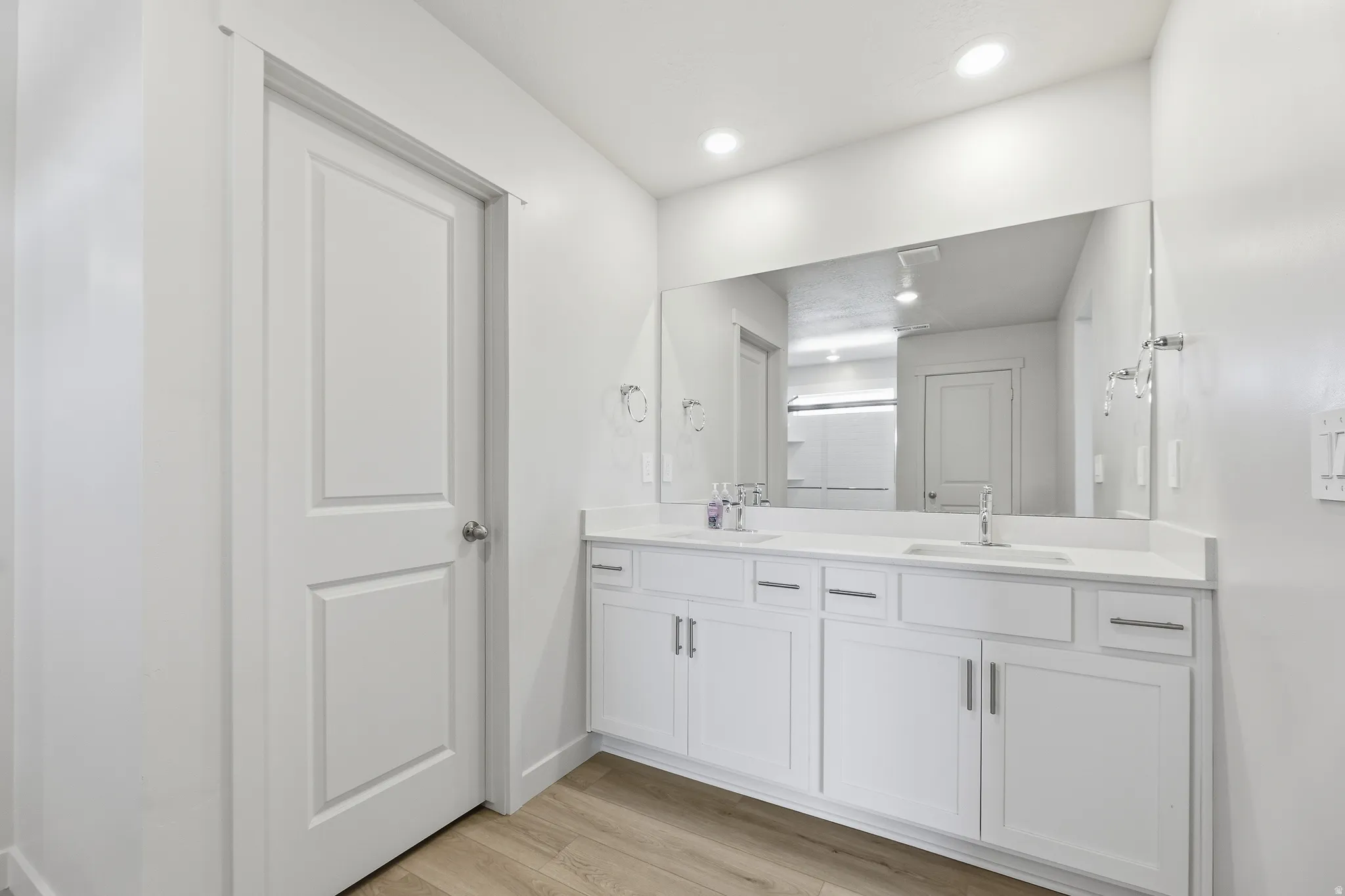 Dual vanity with white cabinetry, light-toned countertops, and wood-finish flooring