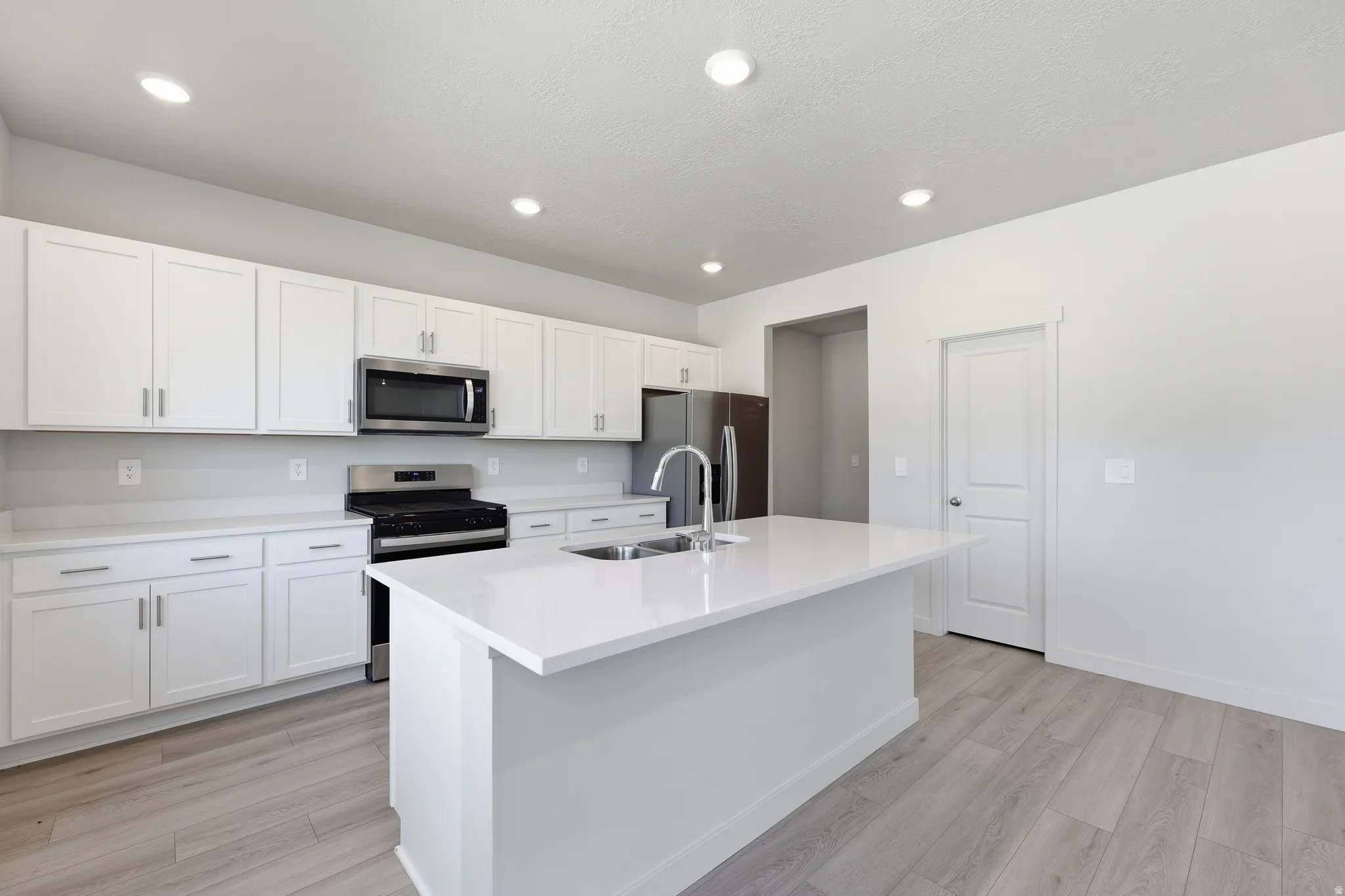 Kitchen featuring white cabinetry, stainless steel appliances, a center island with an integrated sink, recessed lighting, and wood-finish flooring