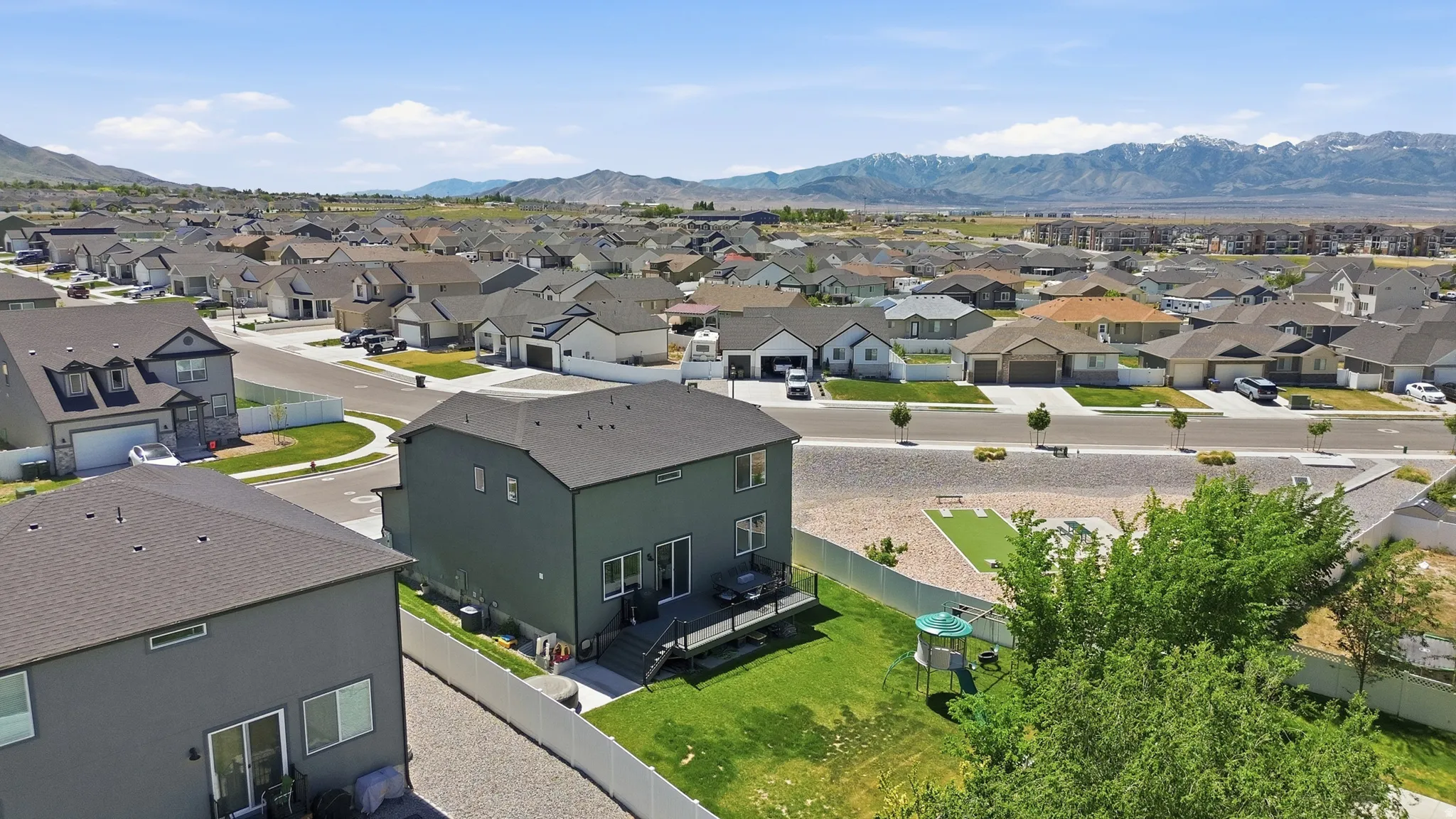 Residential property with a dark gray exterior, featuring a second-story deck, a fenced backyard with a manicured lawn, and a mountain backdrop