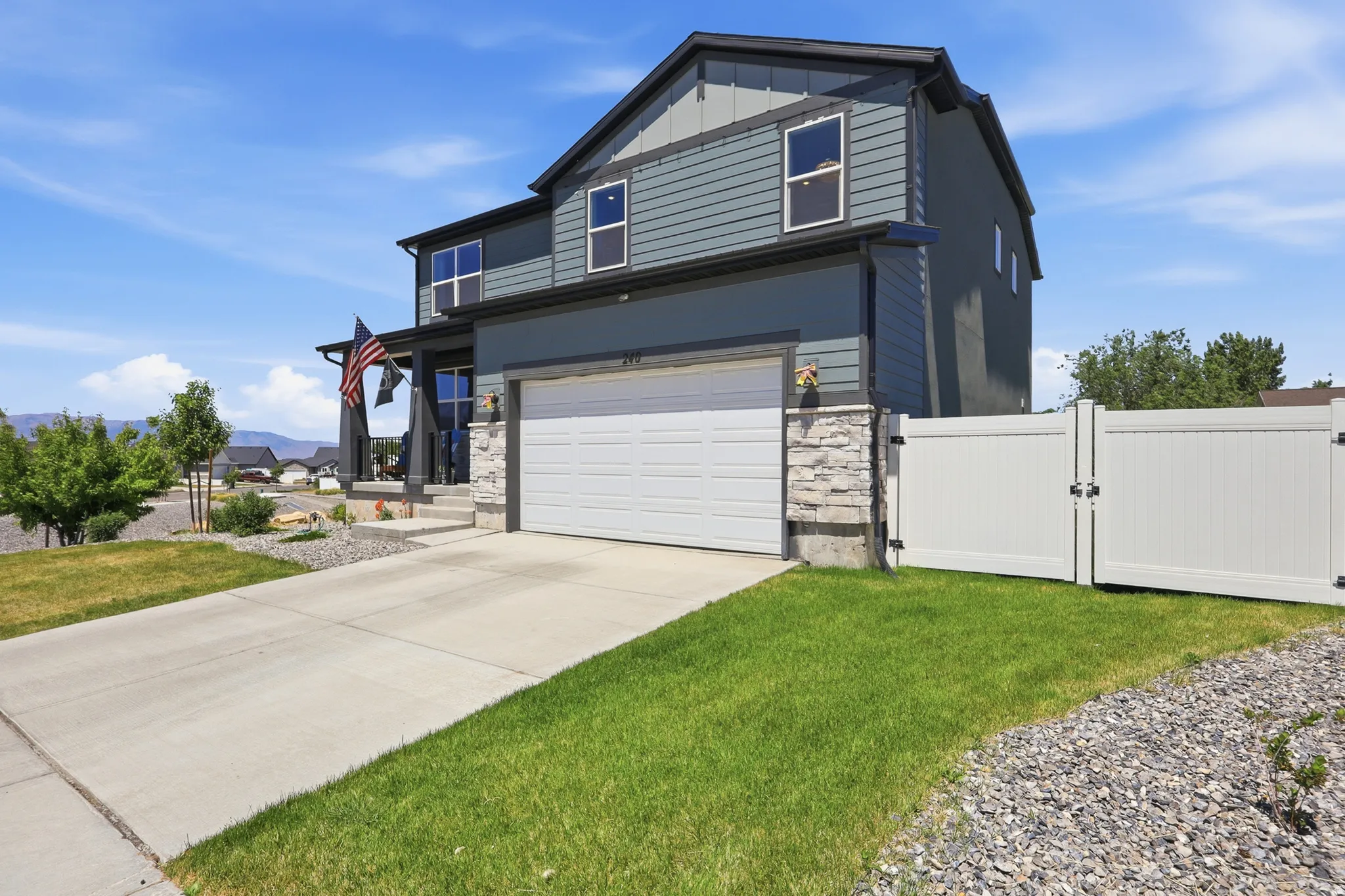 Contemporary two-story exterior featuring a two-car garage, stone veneer accents, a covered front porch, and a white privacy fence