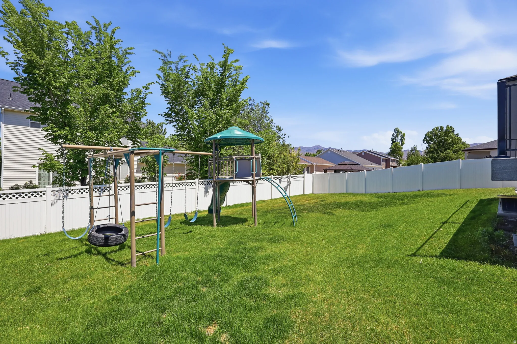Expansive grassy backyard featuring a white privacy fence and established trees