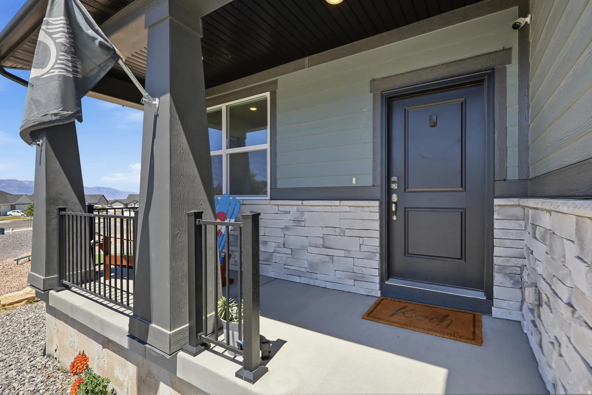 Inviting covered front porch with stone veneer accent, dark paneled entry door, and dark metal railing