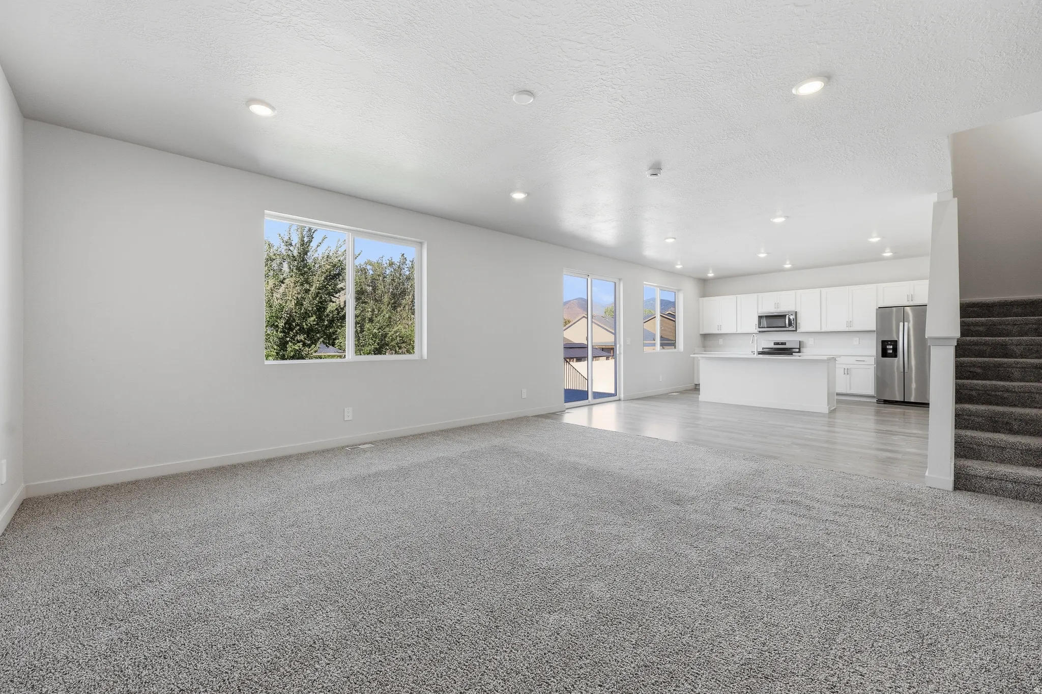 Open-concept layout featuring recessed lighting, a modern kitchen with white cabinetry, stainless steel appliances, and a central island