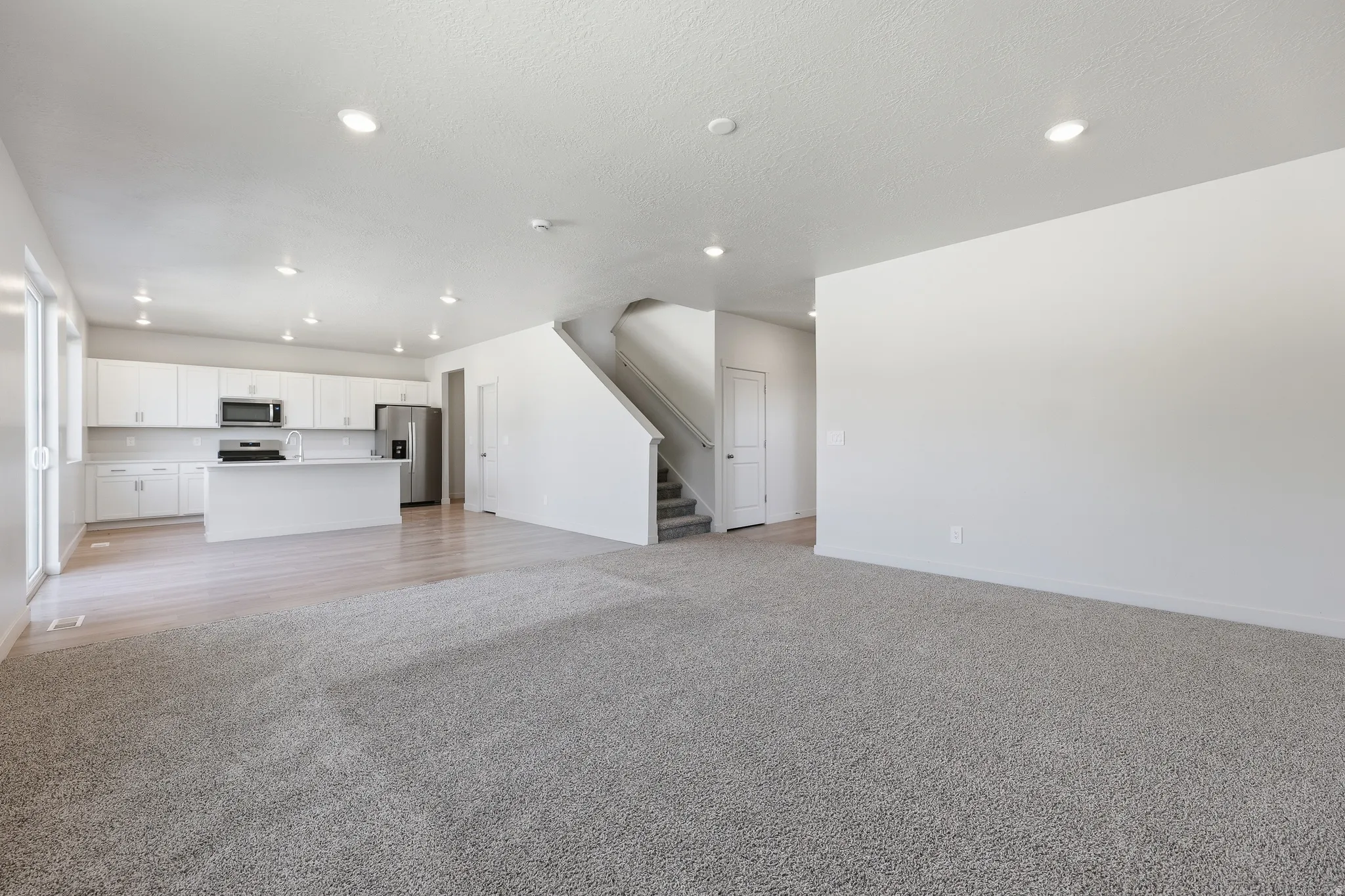 Open-concept living area featuring light wood-finish flooring, light gray carpeting, and white walls