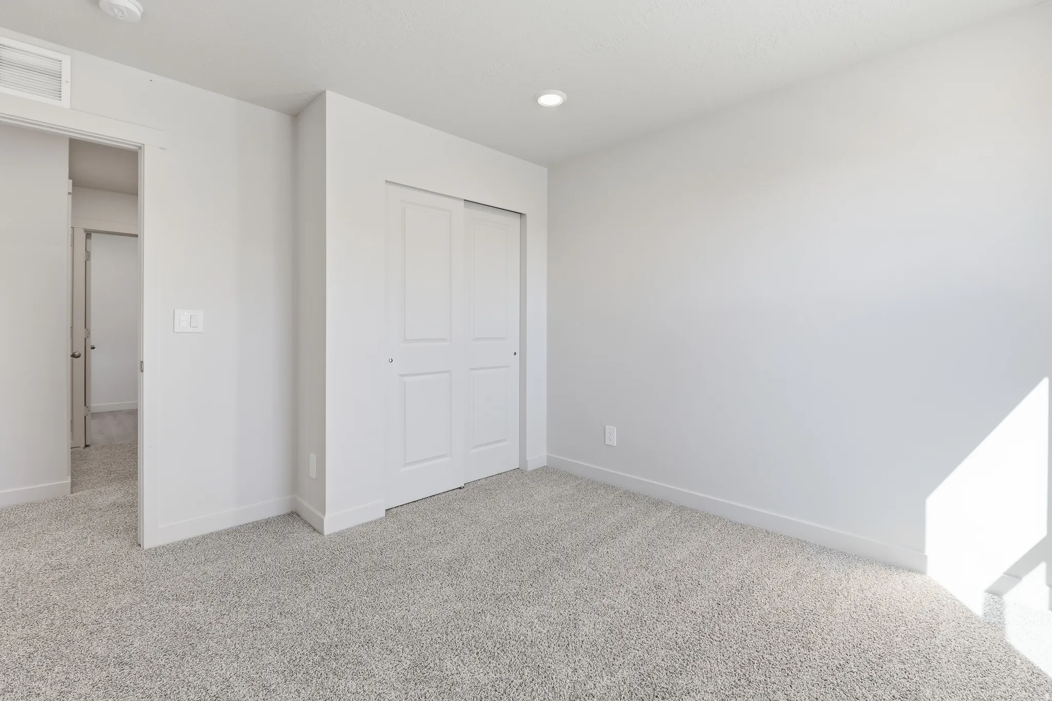 Plush gray carpeting, recessed ceiling lighting, and a sliding panel closet door