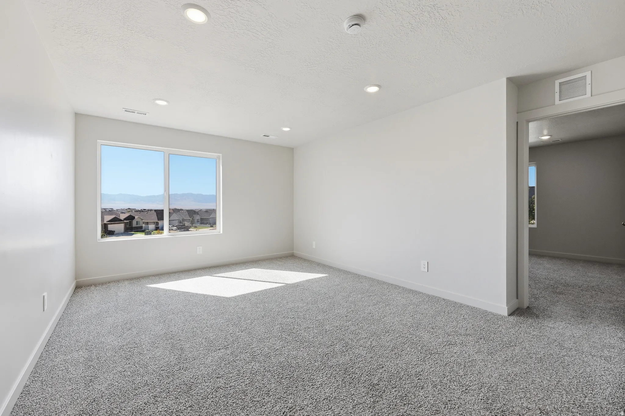Recessed ceiling lighting, window with mountain scenery, neutral wall tones, gray carpeting, and a doorway opening to an additional room
