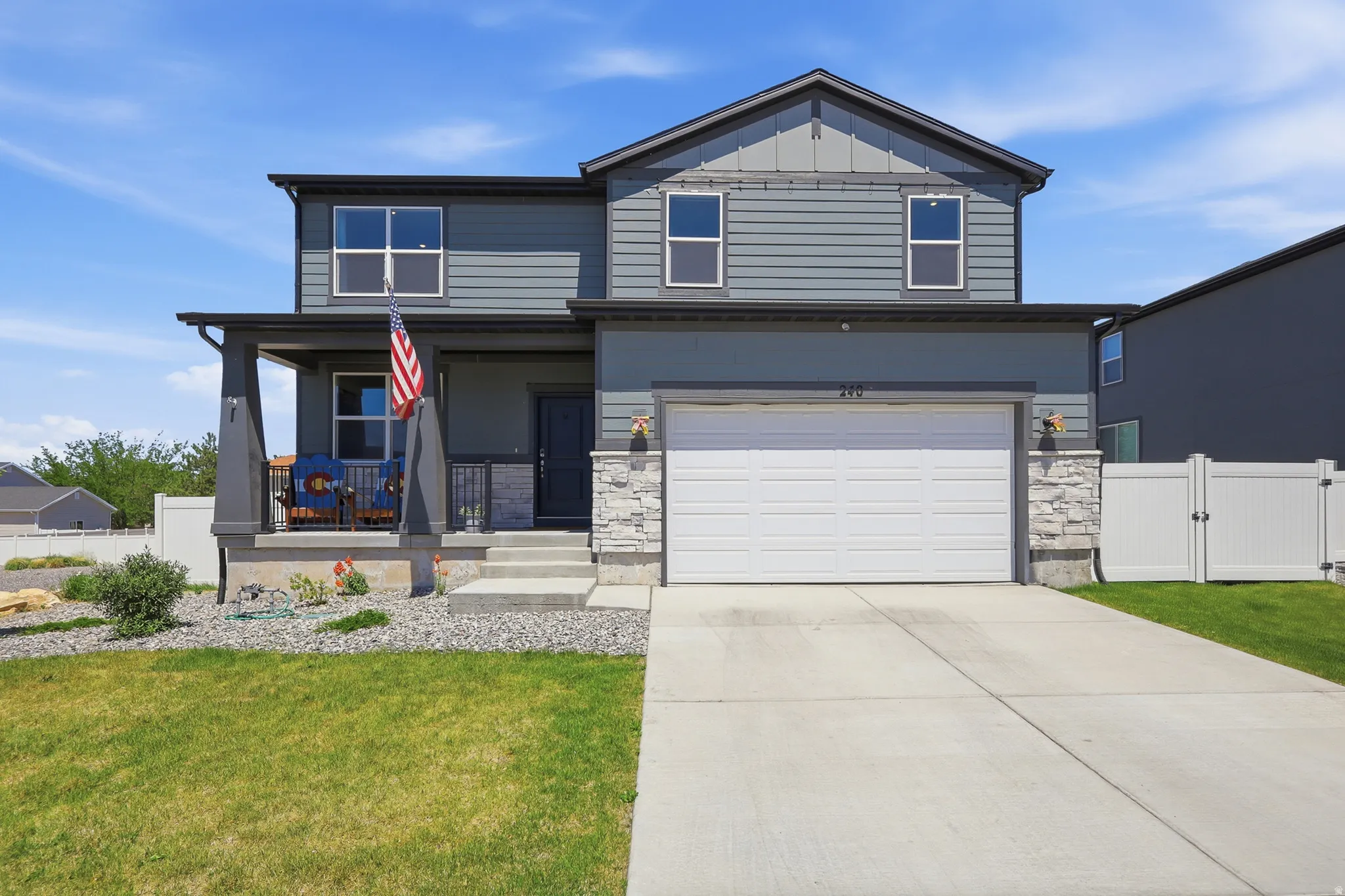 Two-story residence featuring a covered front porch, an attached garage, a concrete driveway, a white vinyl fence, and a landscaped front yard with grass and decorative rock