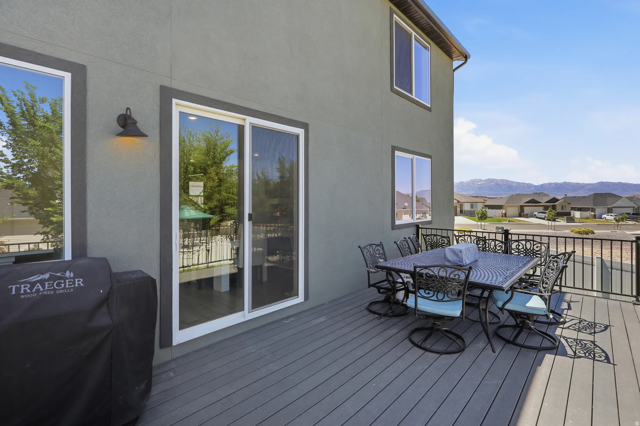 Elevated composite deck featuring a sliding glass door, exterior lighting fixture, black metal railing, and a distant mountain backdrop