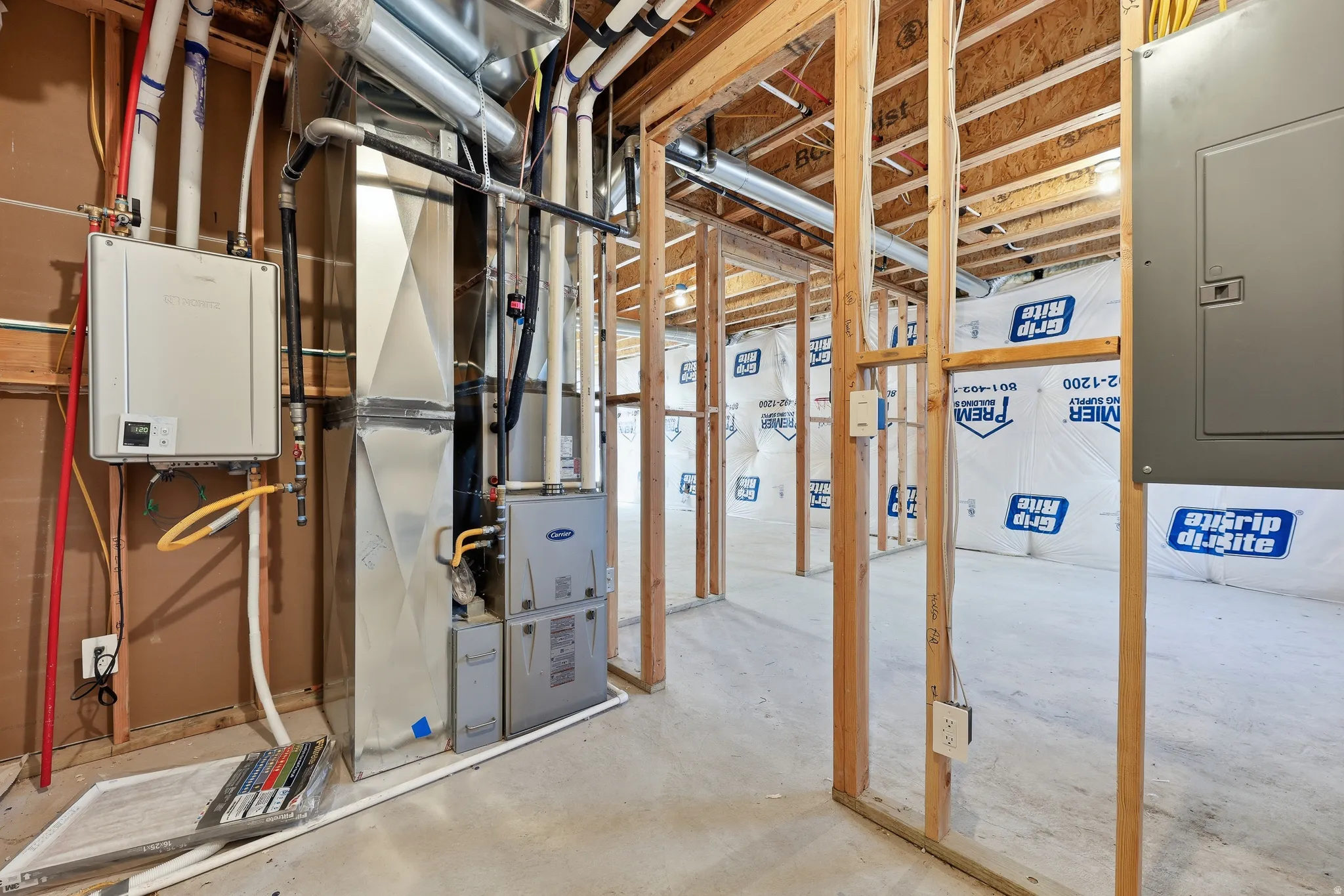 Unfinished basement with concrete flooring and exposed wood framing, featuring a tankless water heater, furnace, and electrical panel