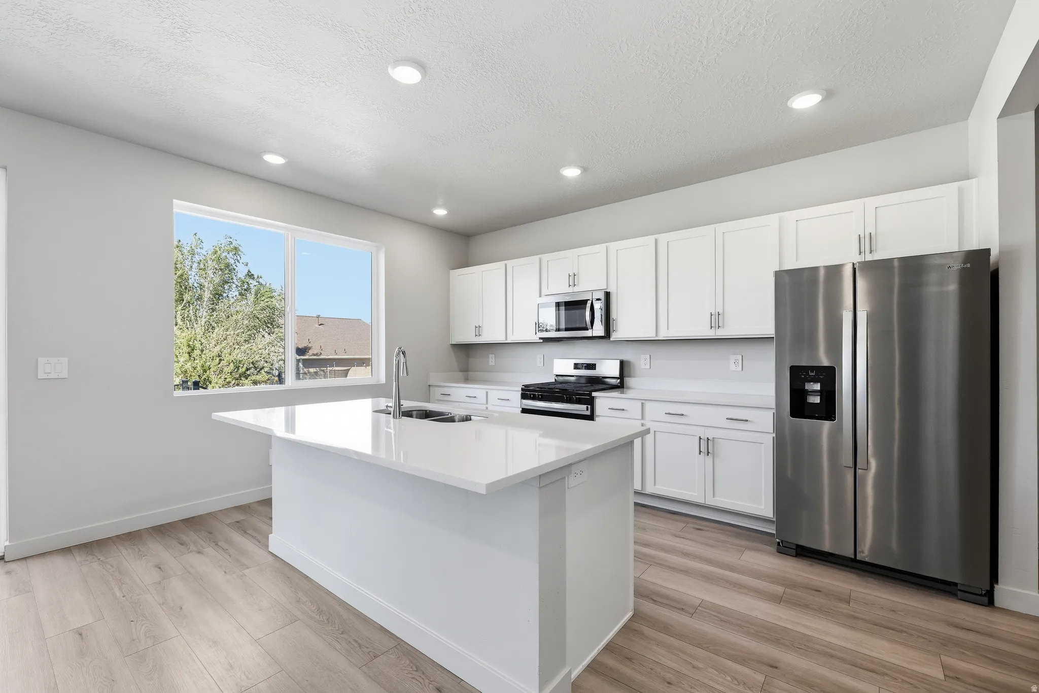 Kitchen featuring an island with an undermount sink, stainless steel appliances, white cabinetry, and wood-finish flooring
