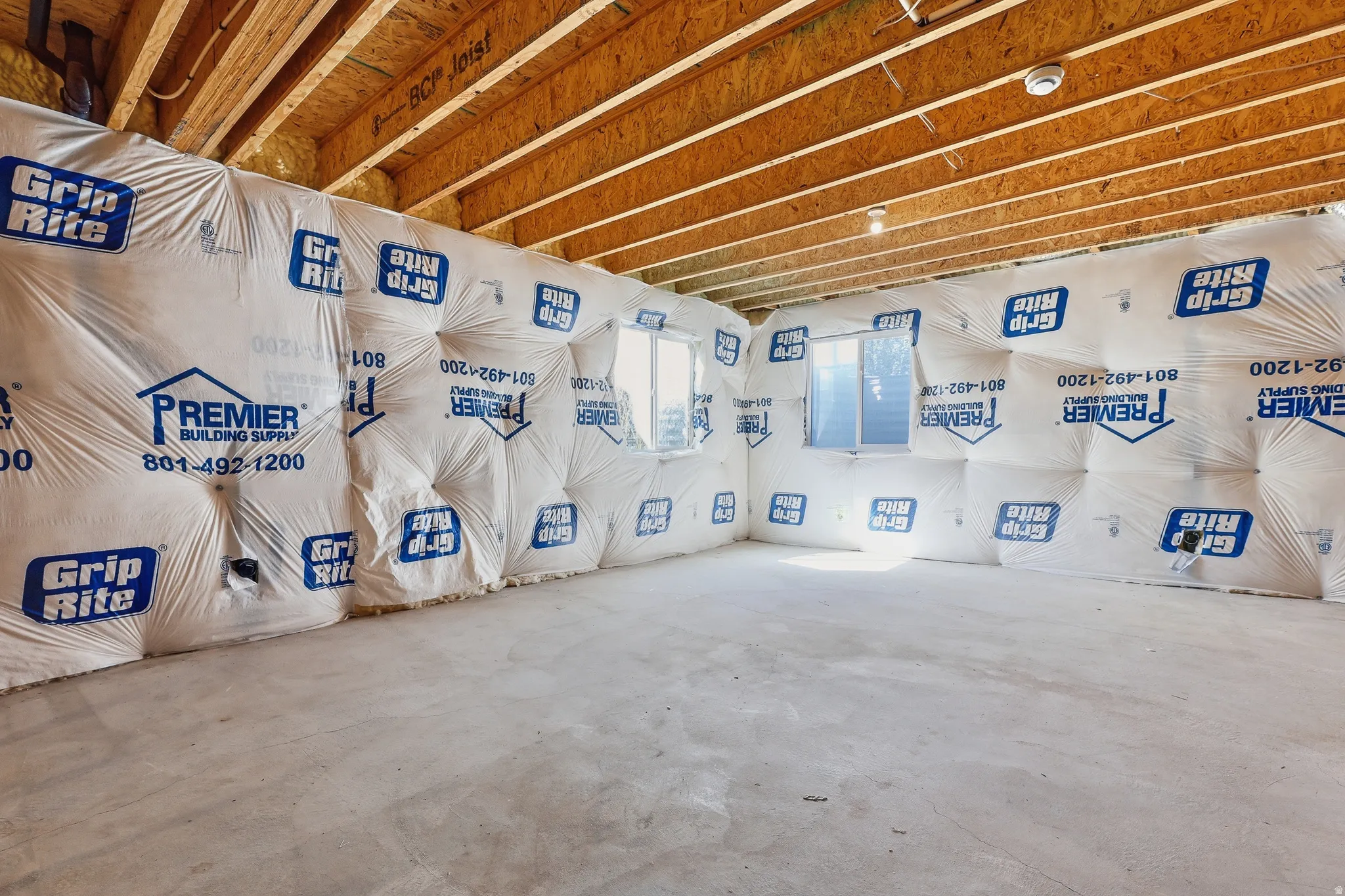 Unfinished room featuring exposed ceiling joists, concrete flooring, insulated walls, and two windows