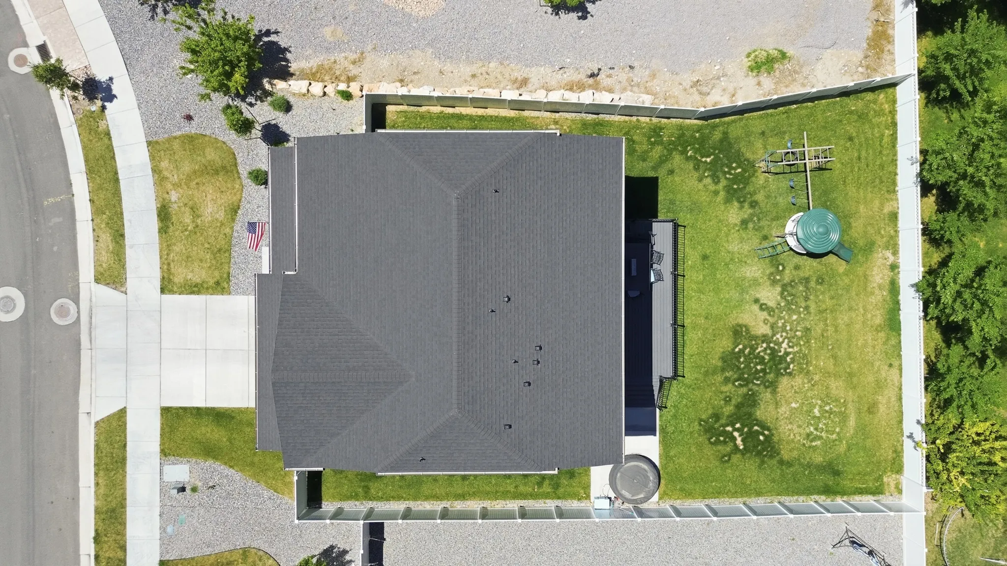 Overhead property view featuring a dark shingle roof, concrete driveway, and a fenced backyard with green lawn
