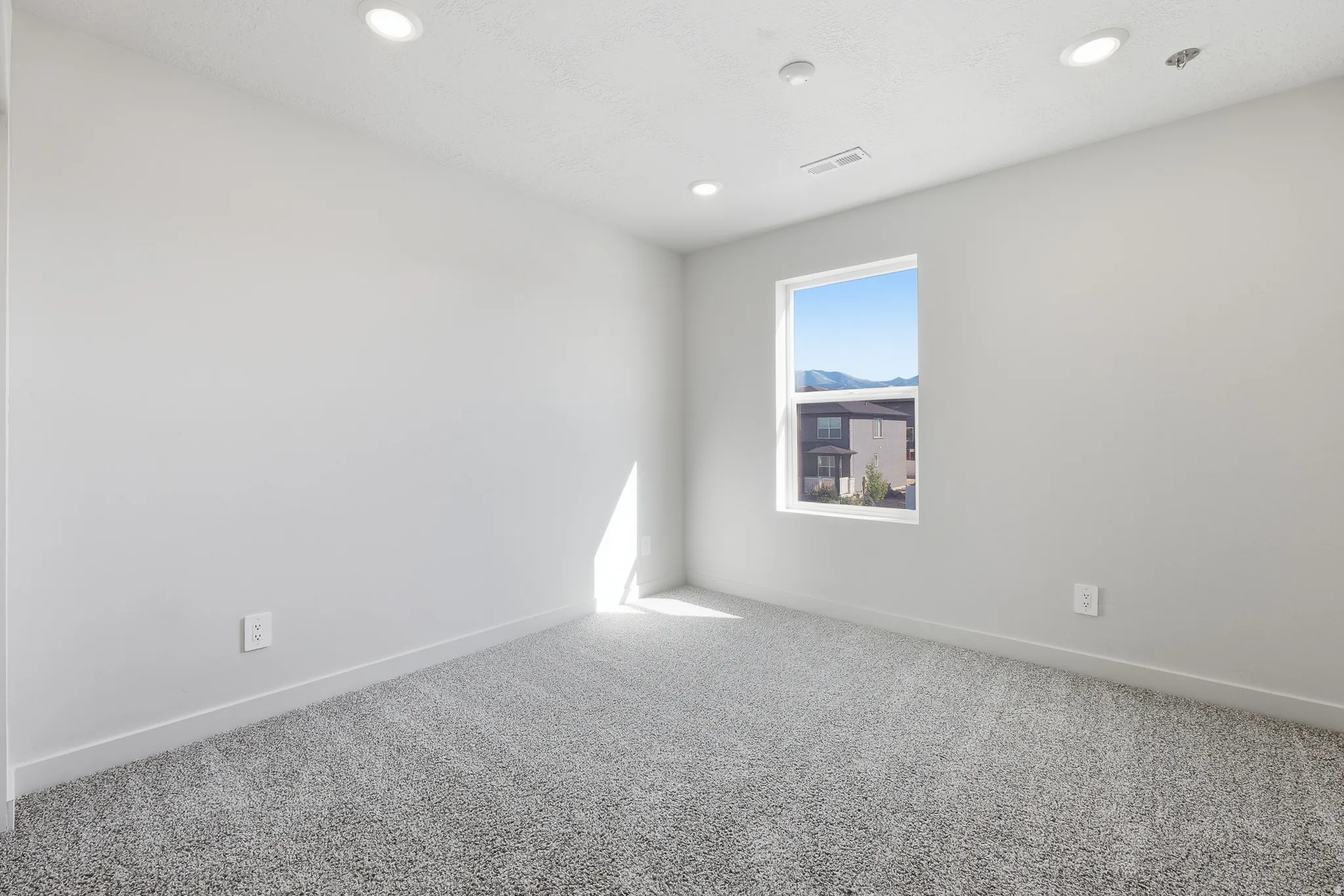 Recessed ceiling lighting, white walls, gray textured carpeting, and a single window with mountain scenery
