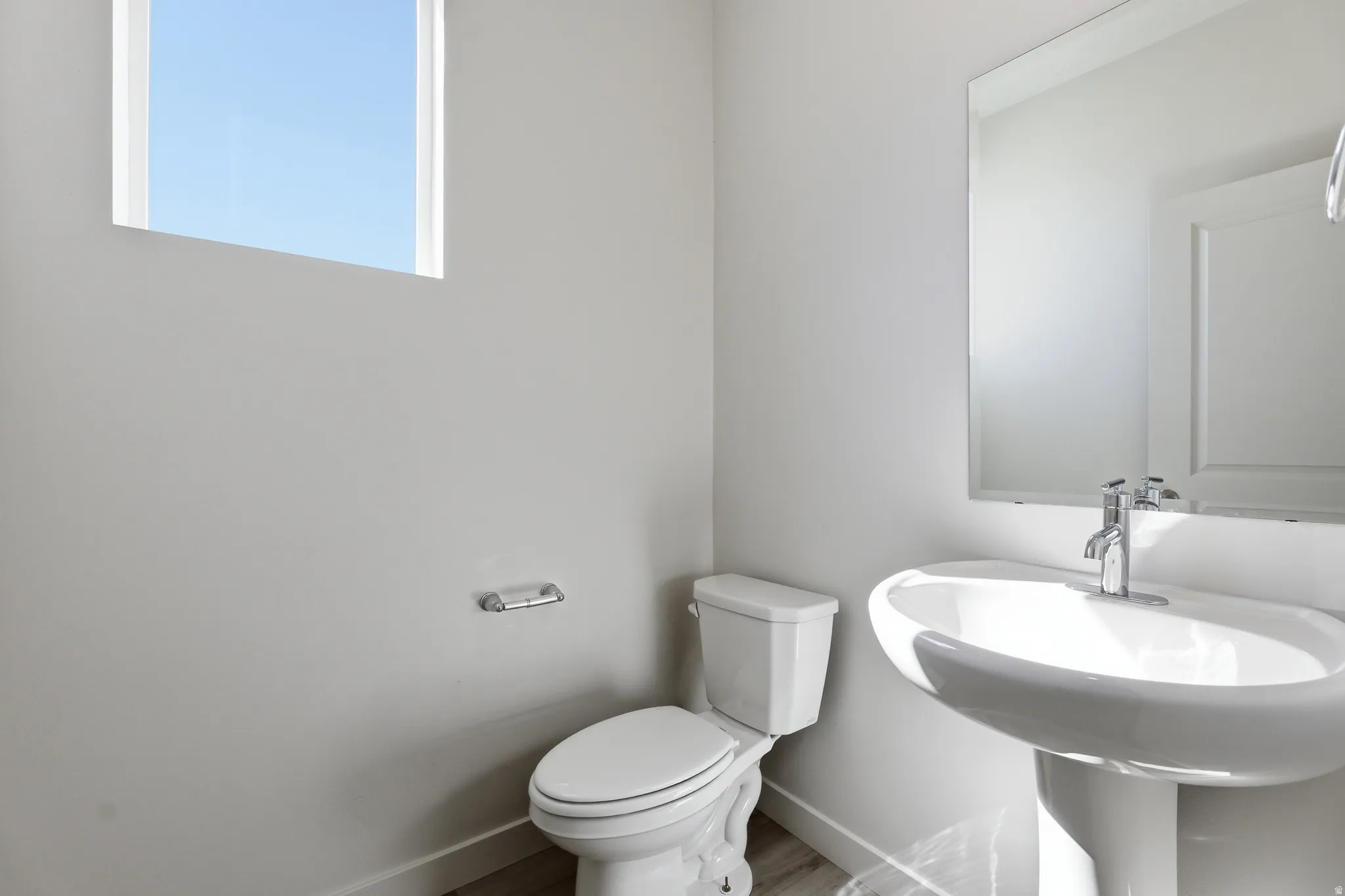 Pedestal sink with chrome faucet, square mirror, and a window with white trim