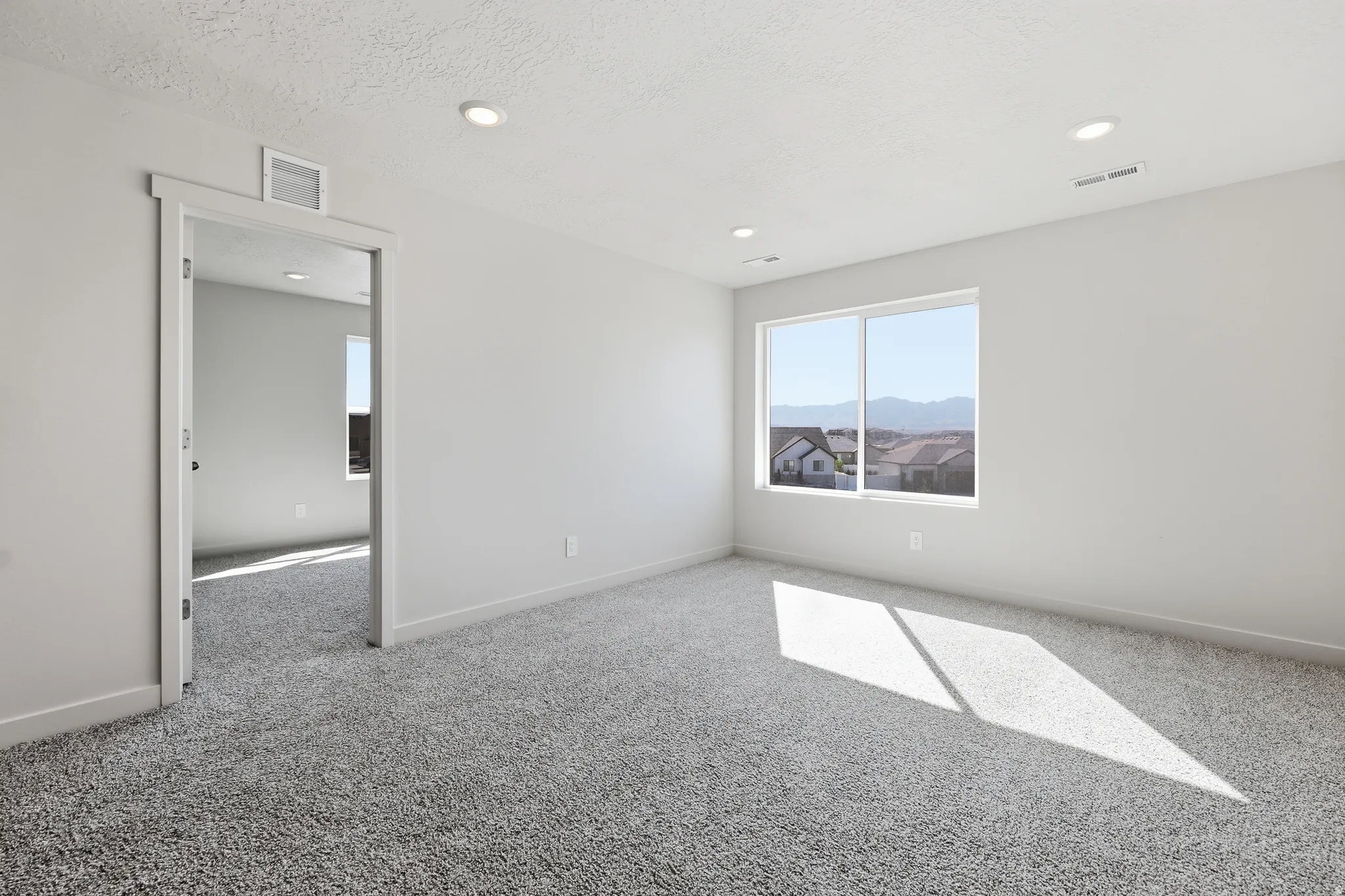 Plush grey carpeting, white painted walls, recessed ceiling lighting, and a large window with a white frame