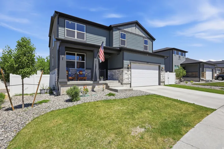 Contemporary two-story residence featuring a covered front porch with iron railings, a two-car garage with a white door, and a stone facade accent
