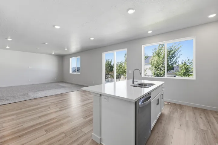 Open-concept living area featuring wood-finish flooring, recessed lighting, and a kitchen island with an integrated sink and stainless steel dishwasher