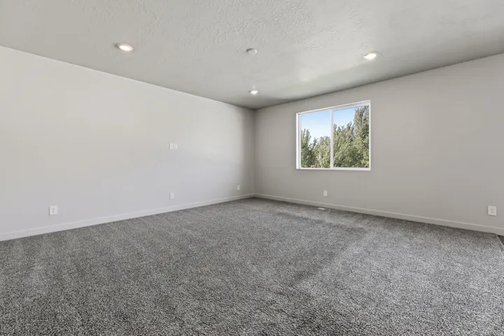 Recessed lighting, light gray walls, textured ceiling, gray carpeting, and a window with a white frame