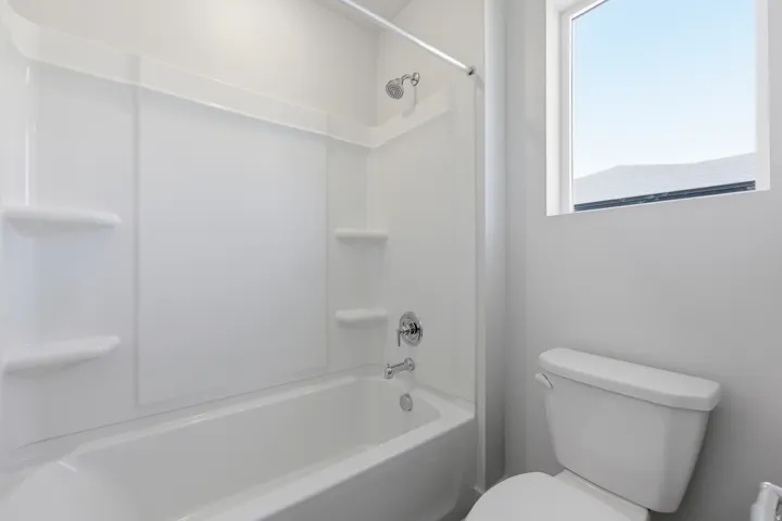 Bathtub and shower combination with white surround, chrome fixtures, and built-in shelving