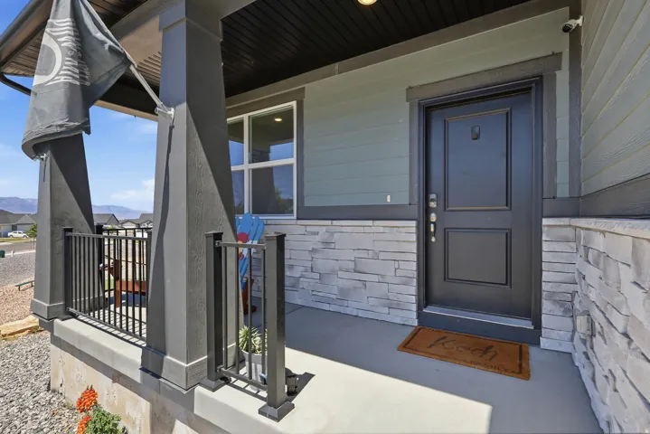 Inviting covered front porch with stone veneer accent, dark paneled entry door, and dark metal railing