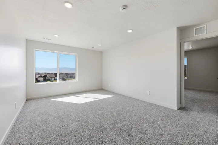 Recessed ceiling lighting, window with mountain scenery, neutral wall tones, gray carpeting, and a doorway opening to an additional room